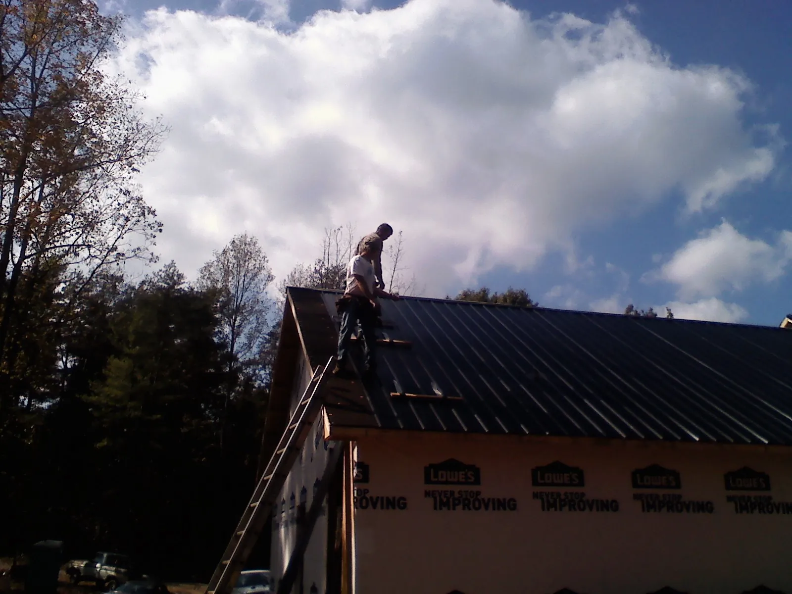 Roofer fastening dark metal panels high against a cloudy sky, from a Roof Inspection job in Santa Cruz