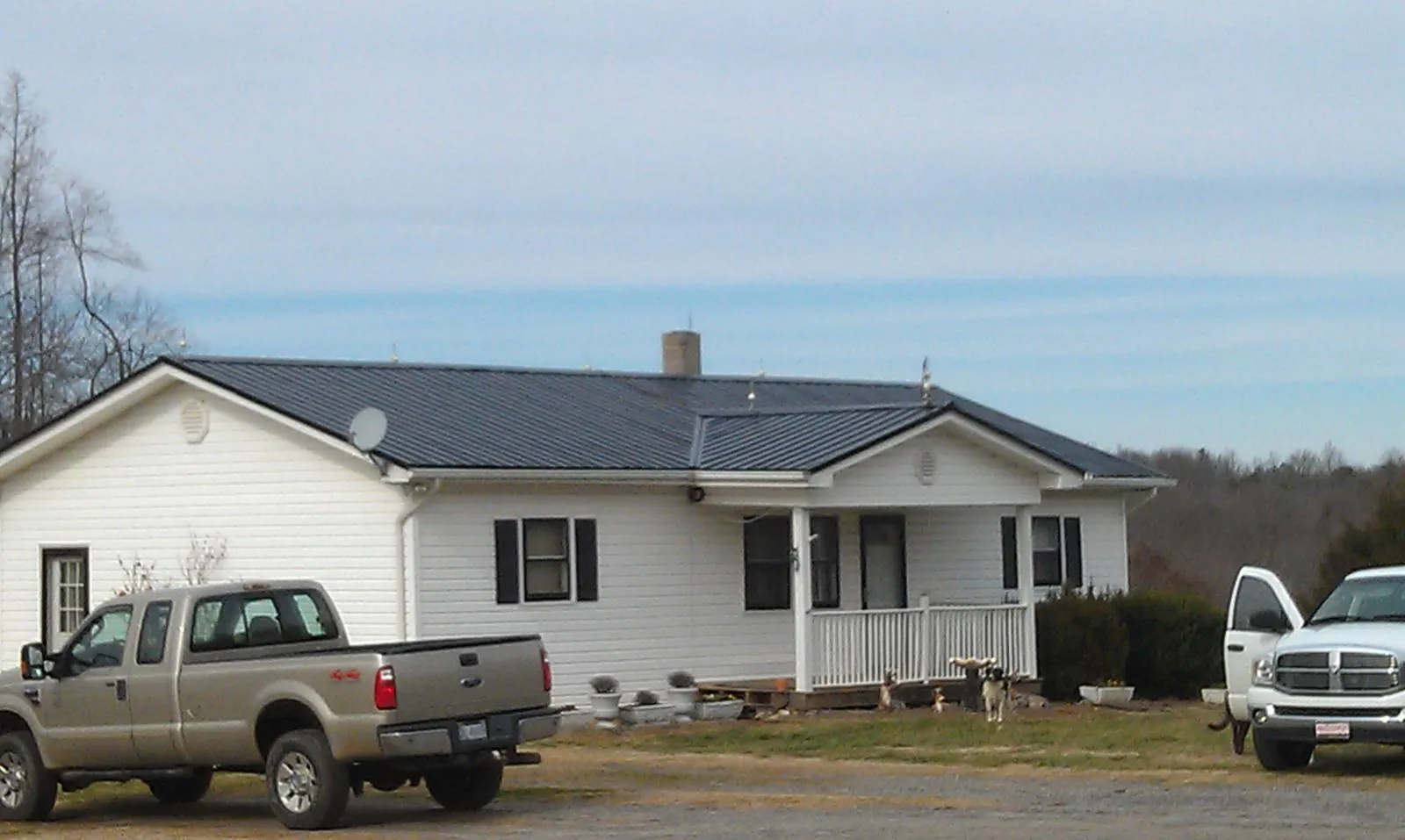 Finished dark metal roof on a white ranch home with work trucks parked in Santa Cruz