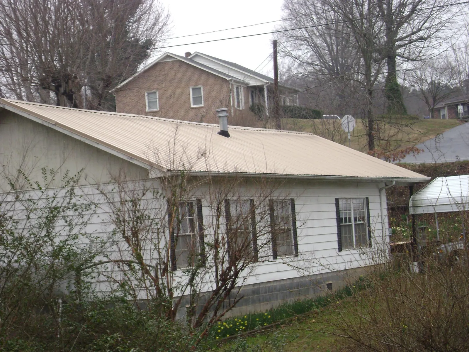 Tan metal roof on a white sided house set into a hillside — Commercial Roofing by Roofing Brothers in Santa Cruz